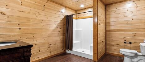 A wooden-paneled bathroom with a shower, toilet, and vanity.