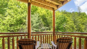 A wooden deck with two Adirondack chairs and a small table, overlooking a forested area. - Mountain Cinema Lodge by Jackson Mountain Rentals (Sevierville)