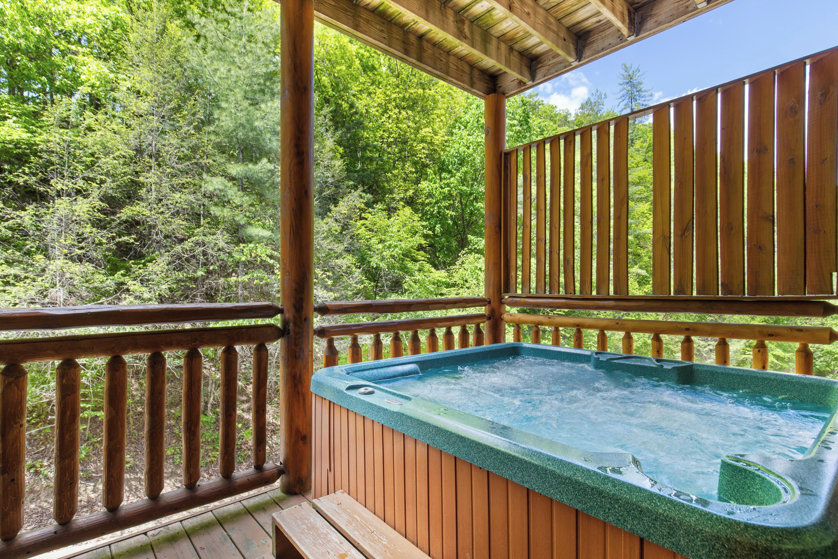 Una terraza de madera con un jacuzzi, rodeada de exuberante vegetación.
