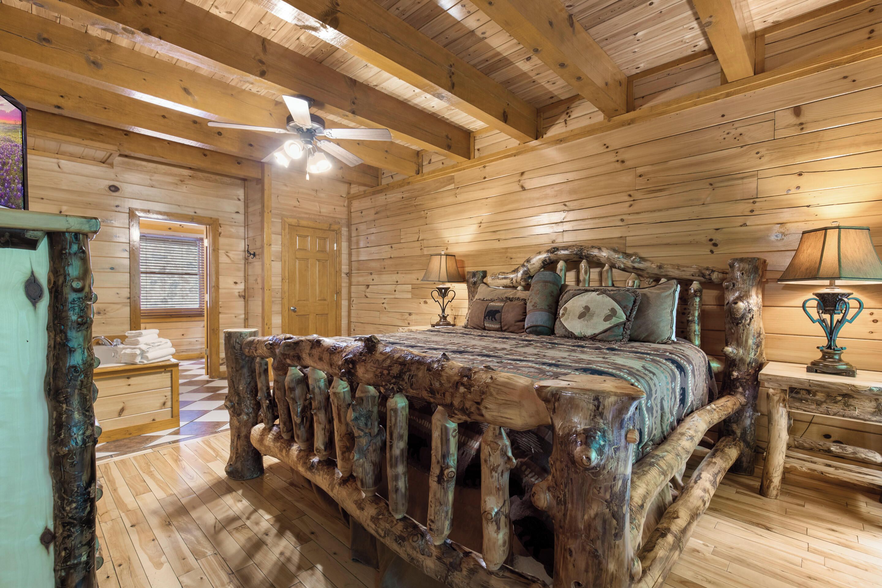 Un dormitorio rústico de cabaña de madera con una cama grande, un ventilador de techo y una ventana con persianas.