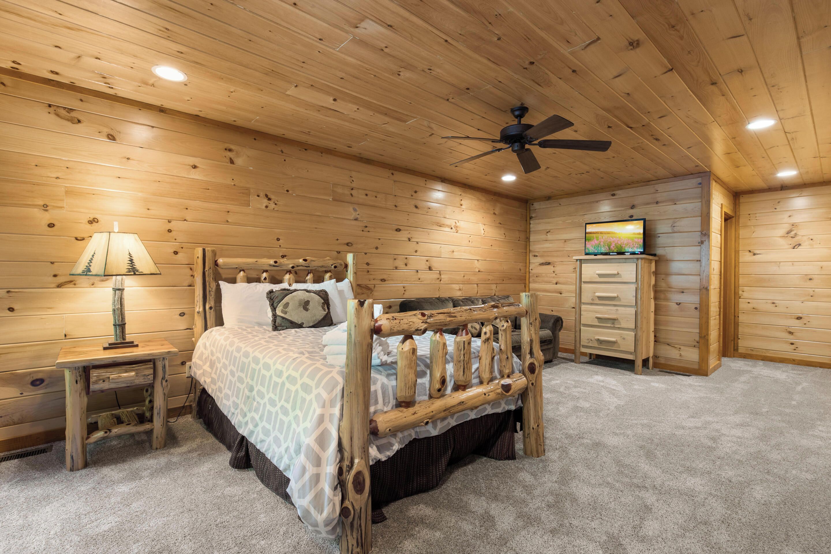 A wooden-paneled bedroom with a bed, a nightstand, a dresser, and a ceiling fan.