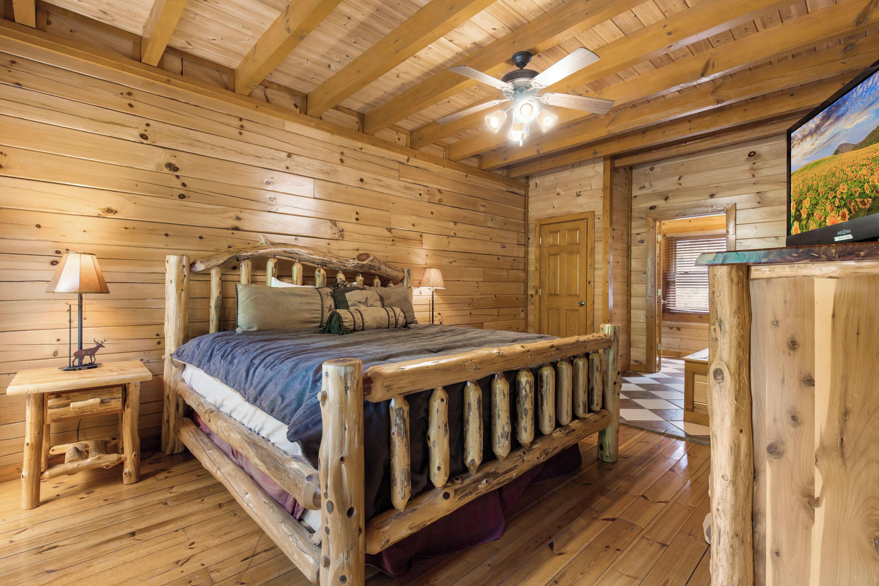 A wooden cabin bedroom with a bed, two nightstands, a ceiling fan, and a television.