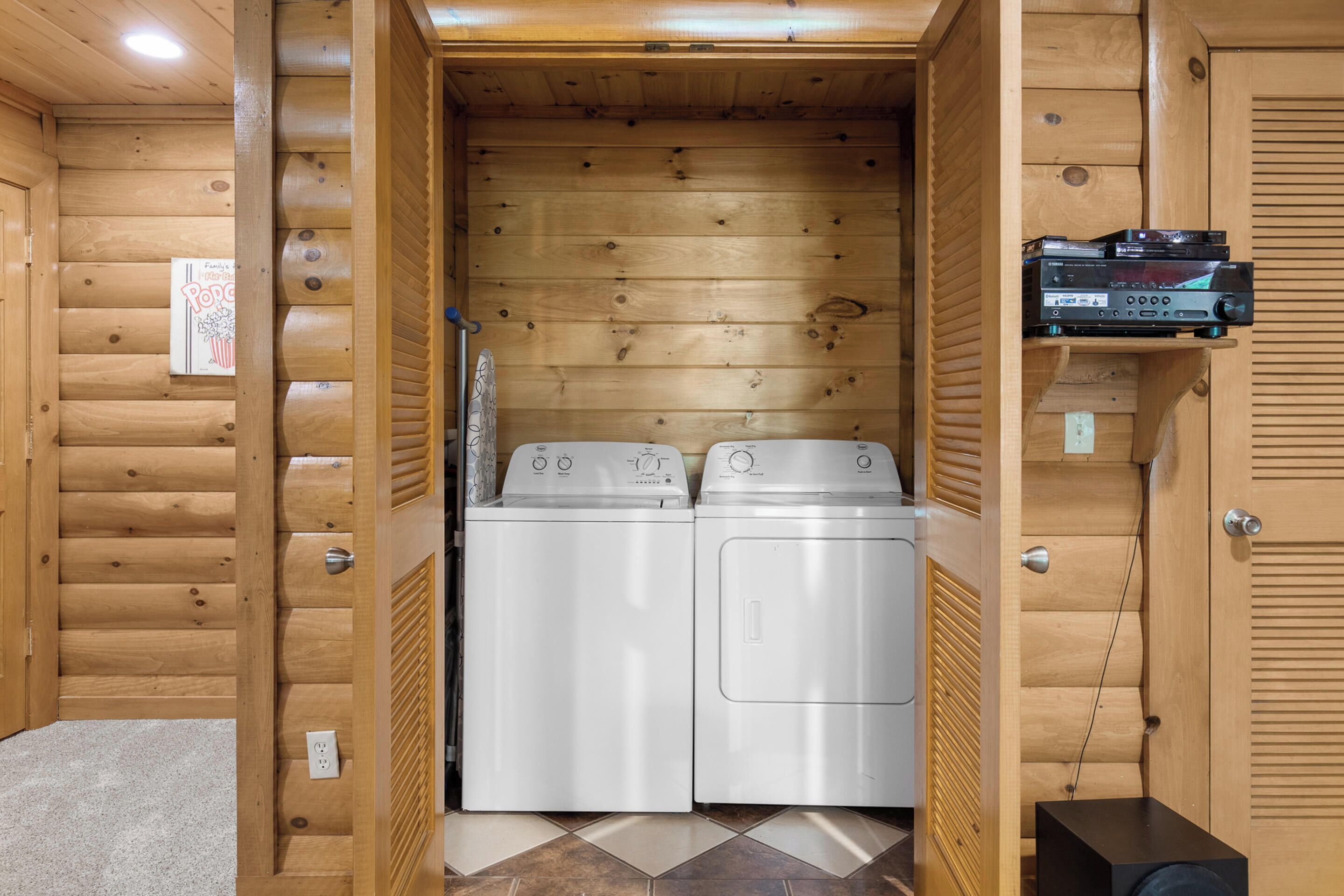 A laundry room with two white washing machines, wooden walls, and a shelf with electronic devices.