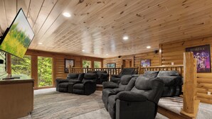 A wooden cabin interior with a large screen, reclining sofas, and a poster on the wall. - Mountain Cinema Lodge by Jackson Mountain Rentals (Sevierville)