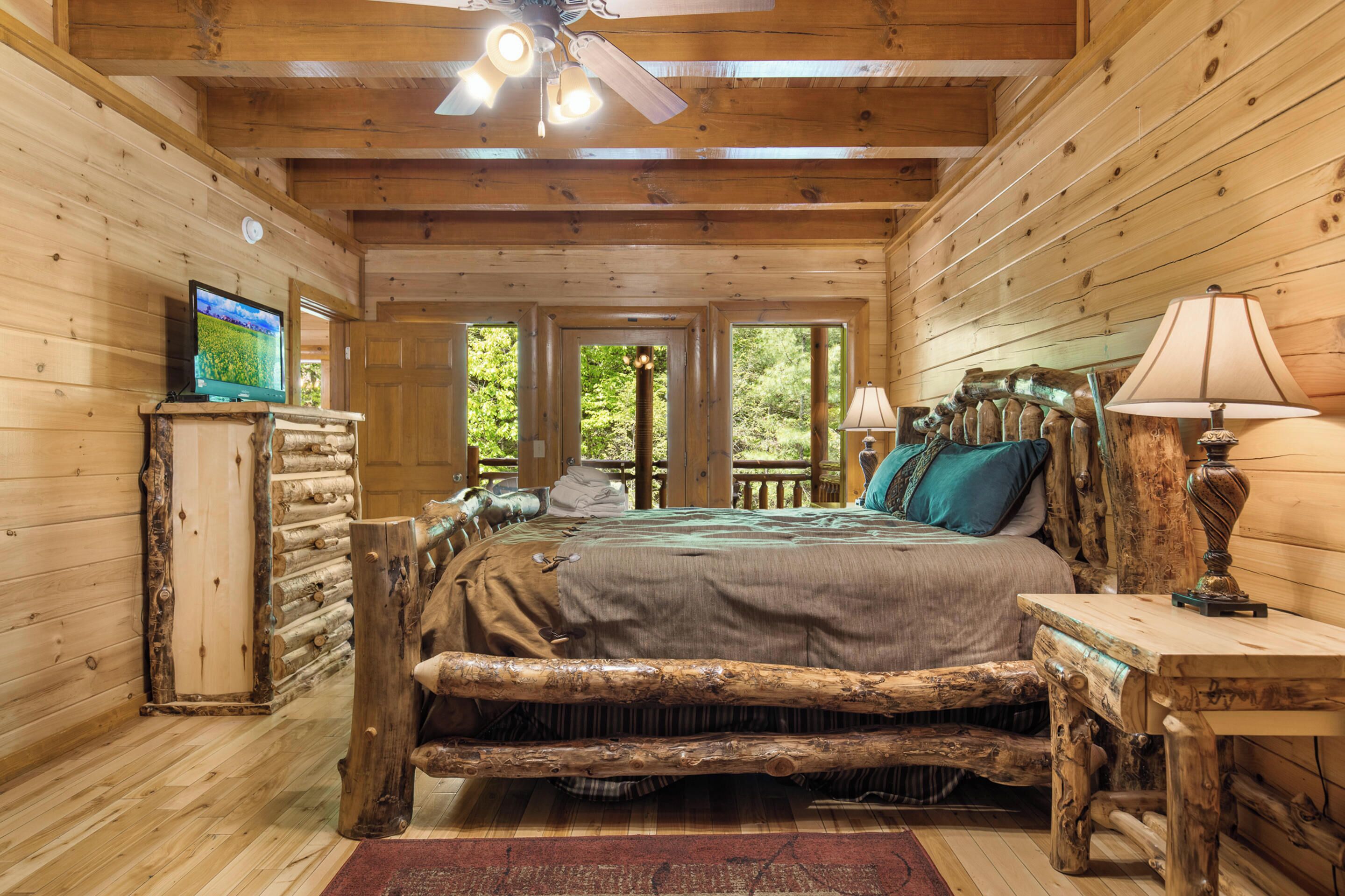 Un dormitorio de cabaña de troncos con una cama, cabecera de madera y un televisor sobre un aparador.