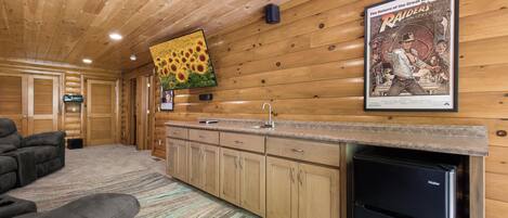 Interior de una cabaña de troncos con cocina, un sofá y un cartel en la pared.