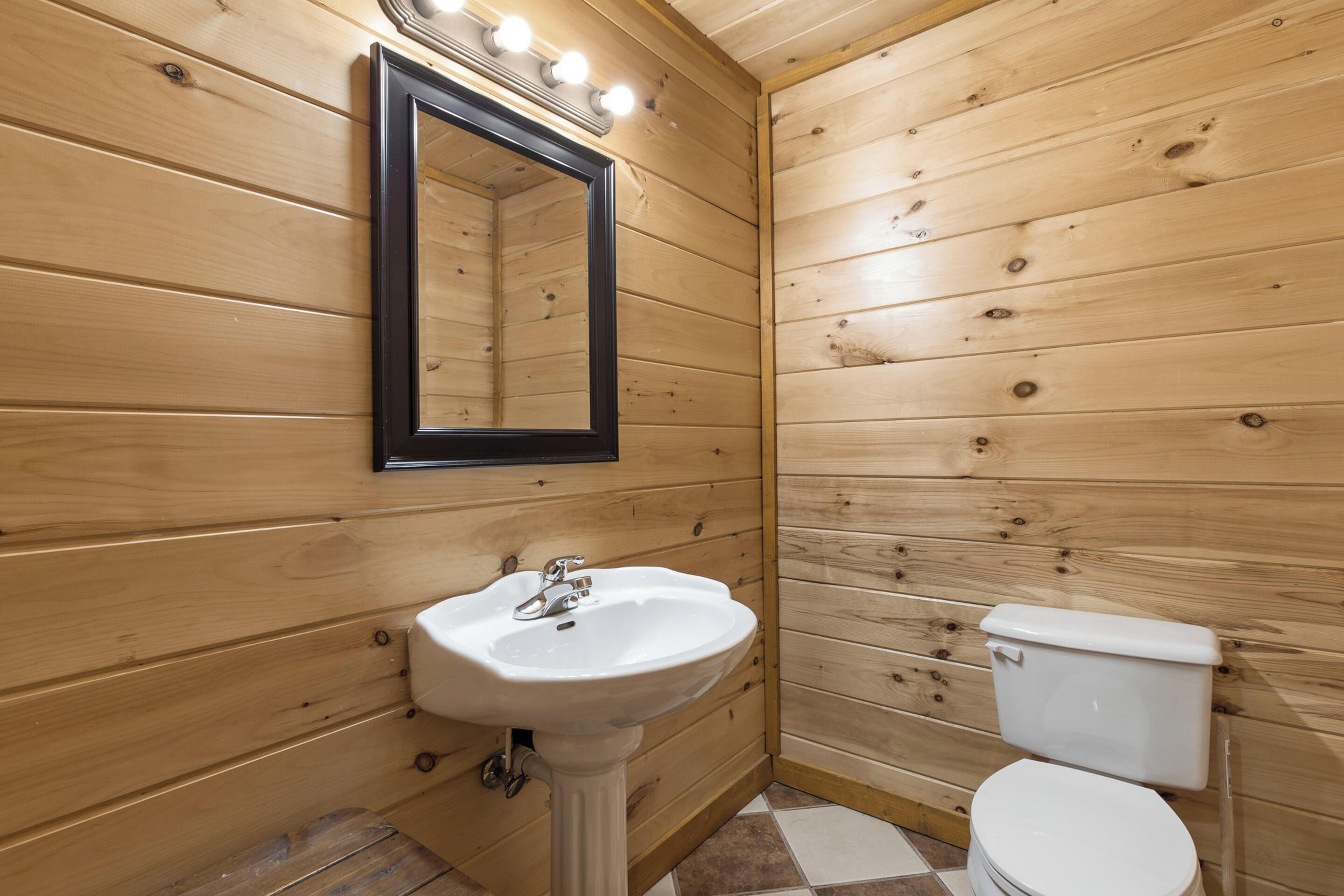 Ein Badezimmer mit Holzwandverkleidung, einem weißen Waschbecken, einem Spiegel und einer Toilette.