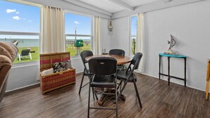 A room with a dining table, chairs, a wicker basket, a clock, and a view of the sea. - Little Cove Resort by Miss Kitty’s (Taft)