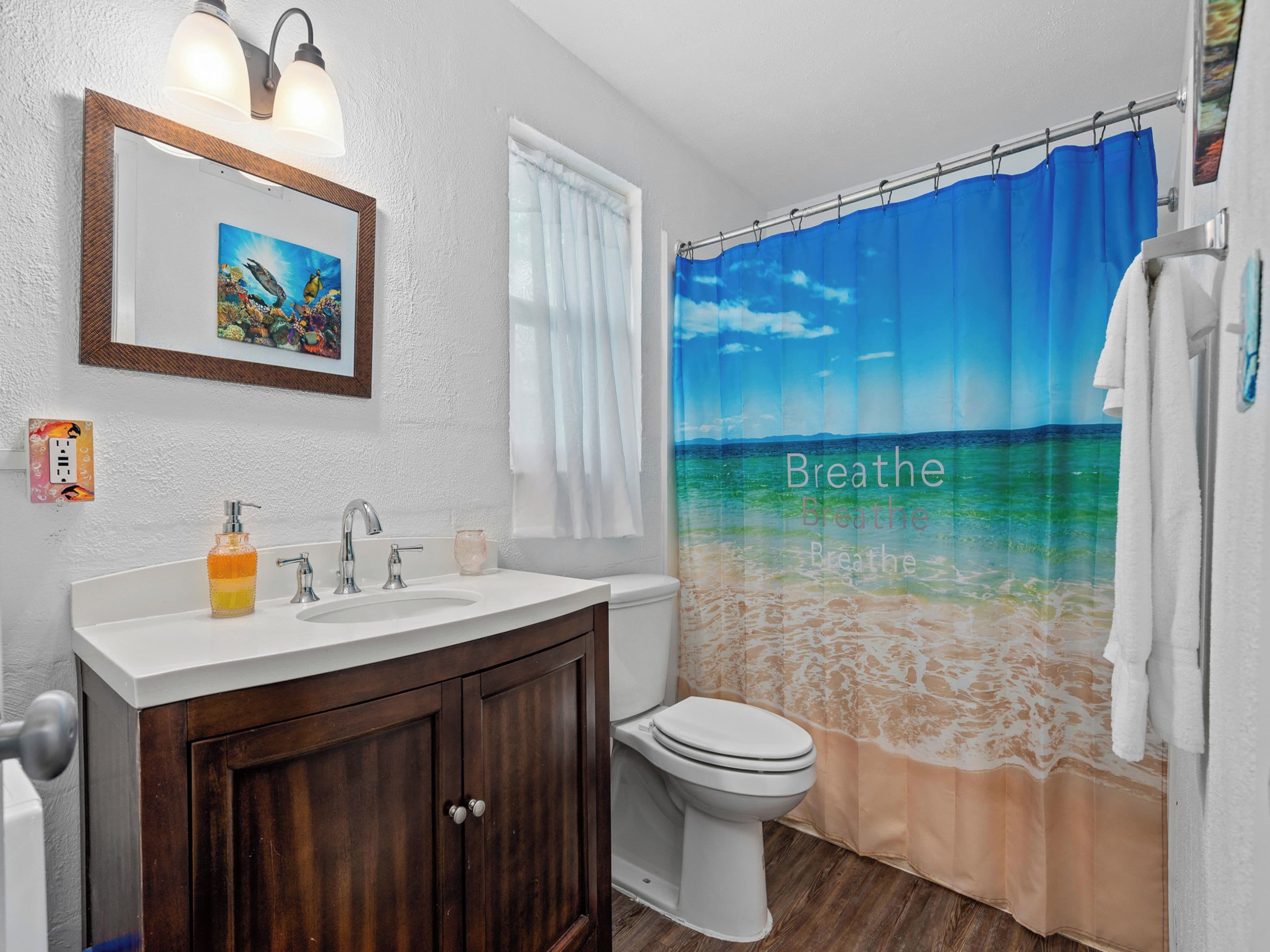 Une salle de bain avec un rideau de douche représentant une scène de plage, un lavabo avec un distributeur de savon et des toilettes.
