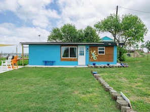 A small, single-story house with a blue exterior, a wooden front door, and a large window. - Little Cove Resort by Miss Kitty’s (Taft)