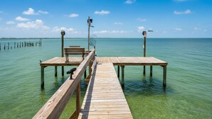 Un muelle de madera que se adentra en aguas claras, con un banco y una silla al final.