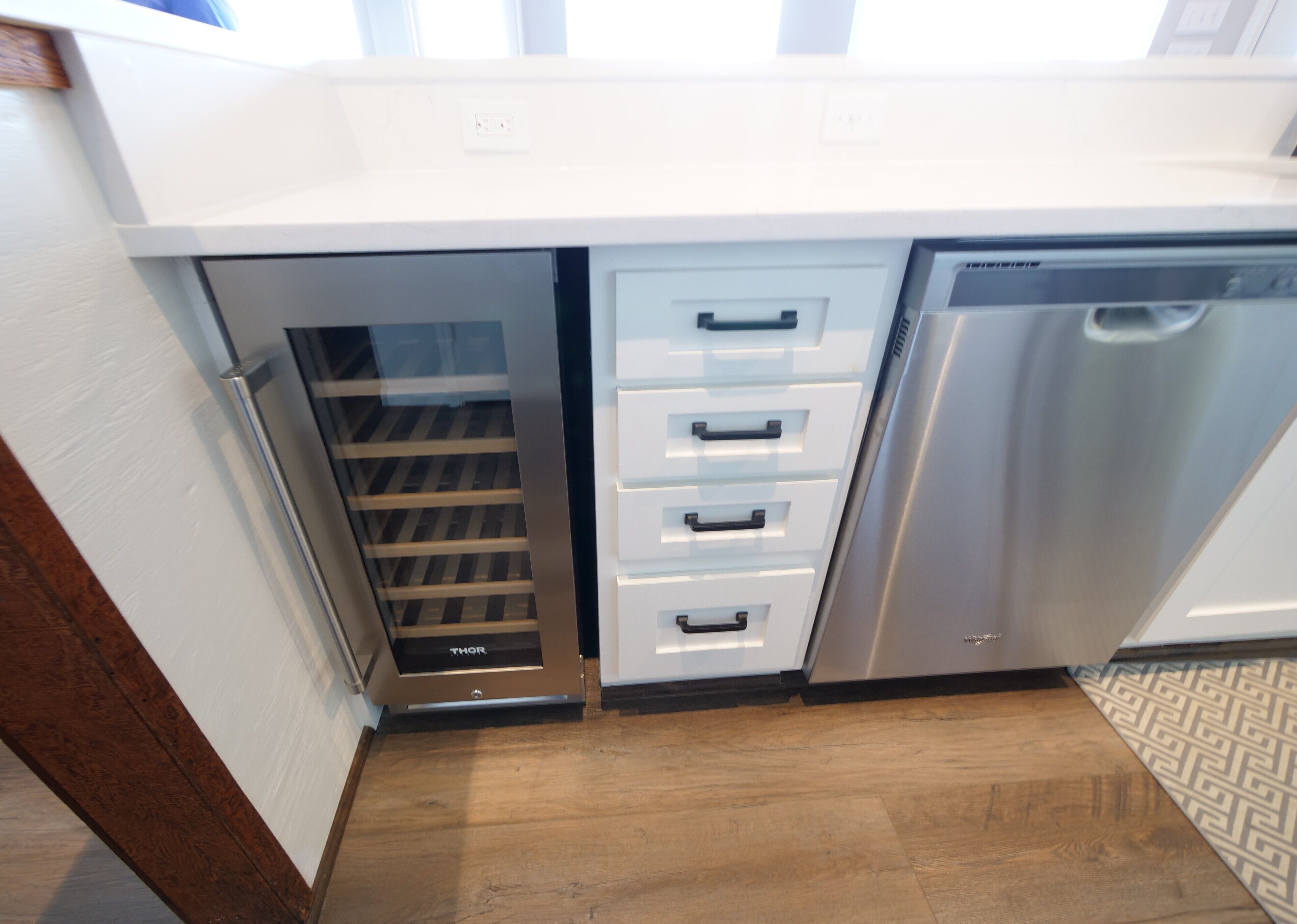 Una cocina con lavavajillas integrado, armarios blancos y piso de madera.