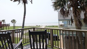 A wooden deck with two chairs, a view of the ocean, and a building with a balcony. - Sandcastle at Bermuda Beach by Ryson Vacation Rentals (Galveston)