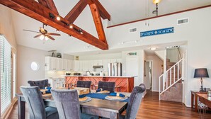 A spacious dining area with a wooden table and chairs, a kitchen in the background, and a staircase leading to another level. - Sandcastle at Bermuda Beach by Ryson Vacation Rentals (Galveston)