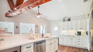 A modern kitchen with white cabinetry, a stainless steel dishwasher, and a wooden ceiling beam. - Sandcastle at Bermuda Beach by Ryson Vacation Rentals (Galveston)