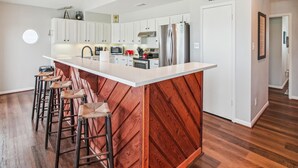 A modern kitchen with a large island, white cabinetry, and a wooden accent wall. - Sandcastle at Bermuda Beach by Ryson Vacation Rentals (Galveston)