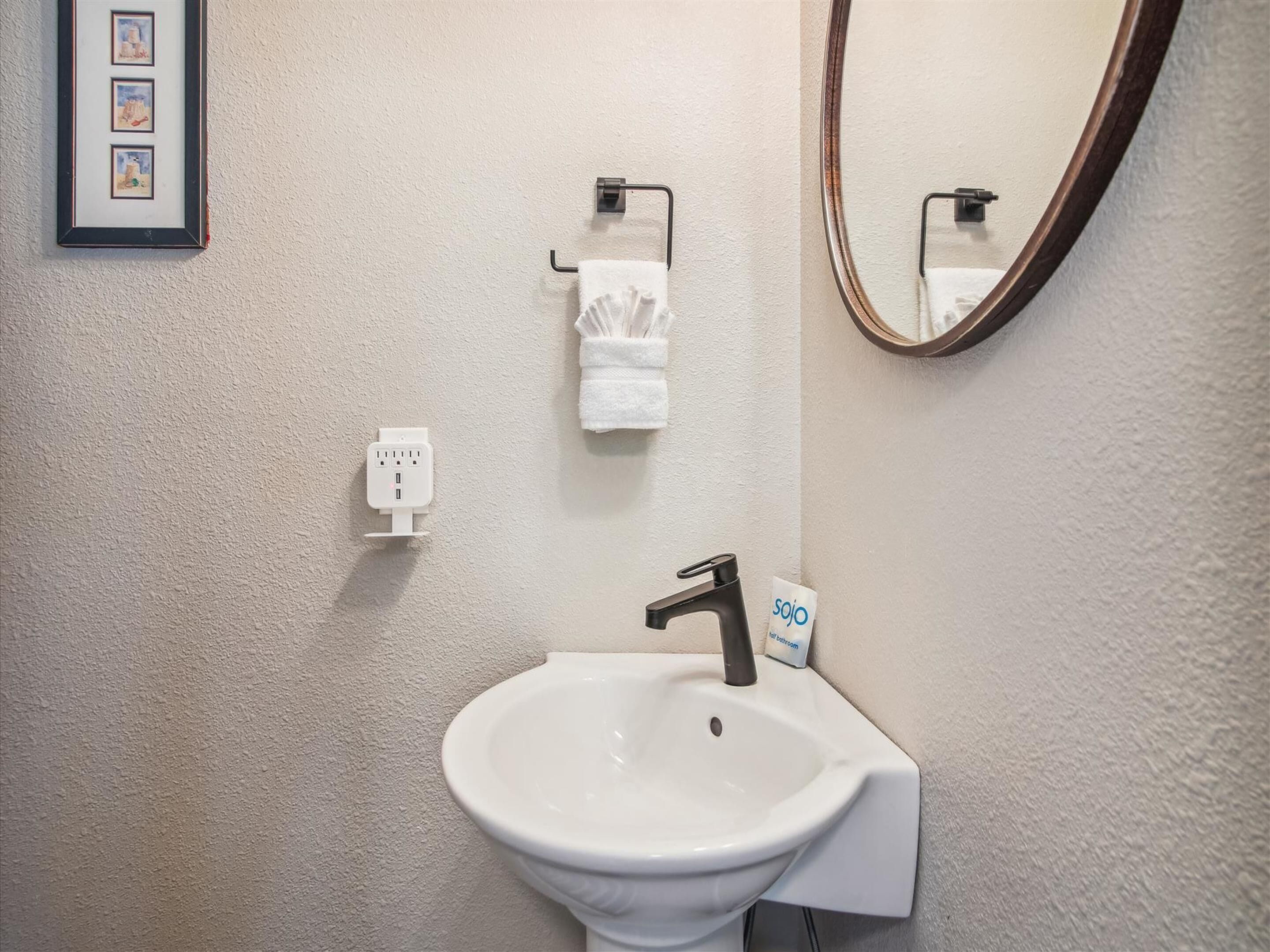Un bagno con un lavandino bianco, uno specchio, un porta asciugamani e una presa di corrente.