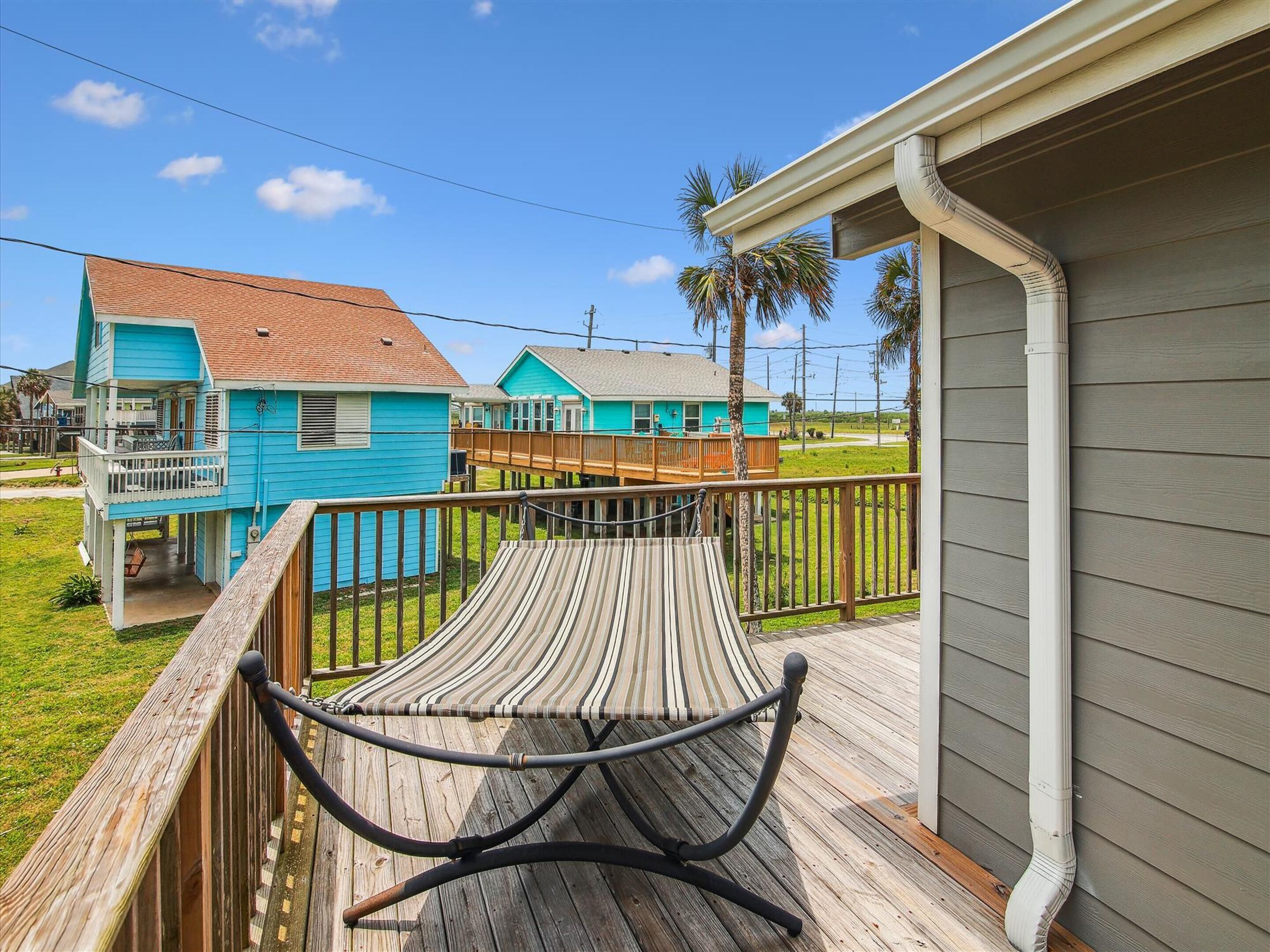 A wooden deck with a hammock, a small porch, and a house with a blue exterior.