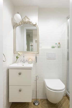 Un baño con un tocador blanco, un espejo con marco ornamentado, un inodoro blanco y una lámpara empotrada en la pared.