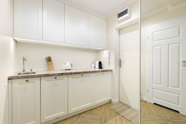 Una cocina con armarios blancos, encimera de mármol y suelo de madera.