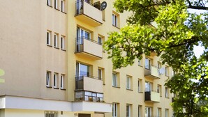 En flervåningsbyggnad med bostäder, balkonger, en grind vid entrén och parkerade bilar längs gatan.