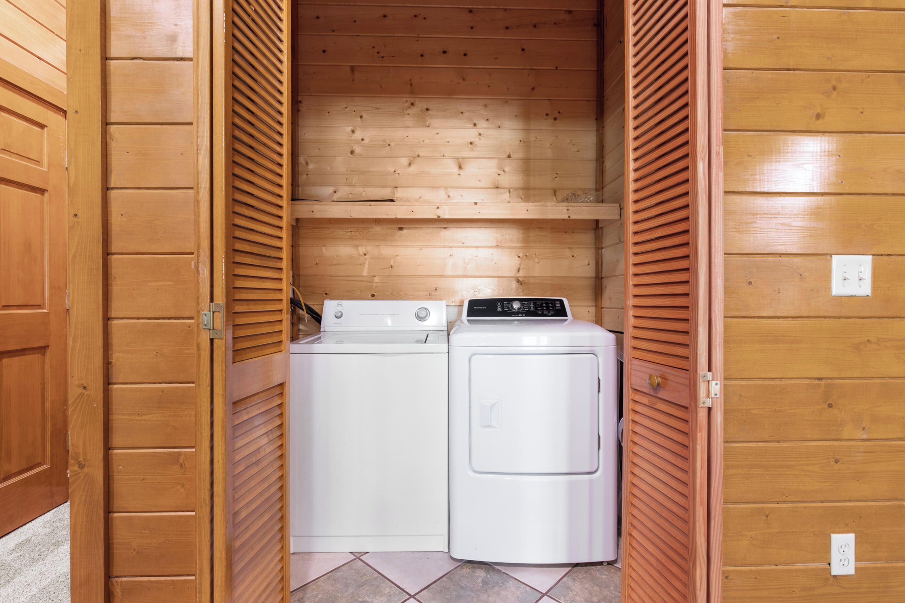 A laundry room with two white washing machines and a dryer, wooden walls, and a tiled floor.