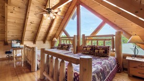 Quarto de cabana de madeira com uma cama grande, cabeceira de madeira, uma escrivaninha e uma cadeira.