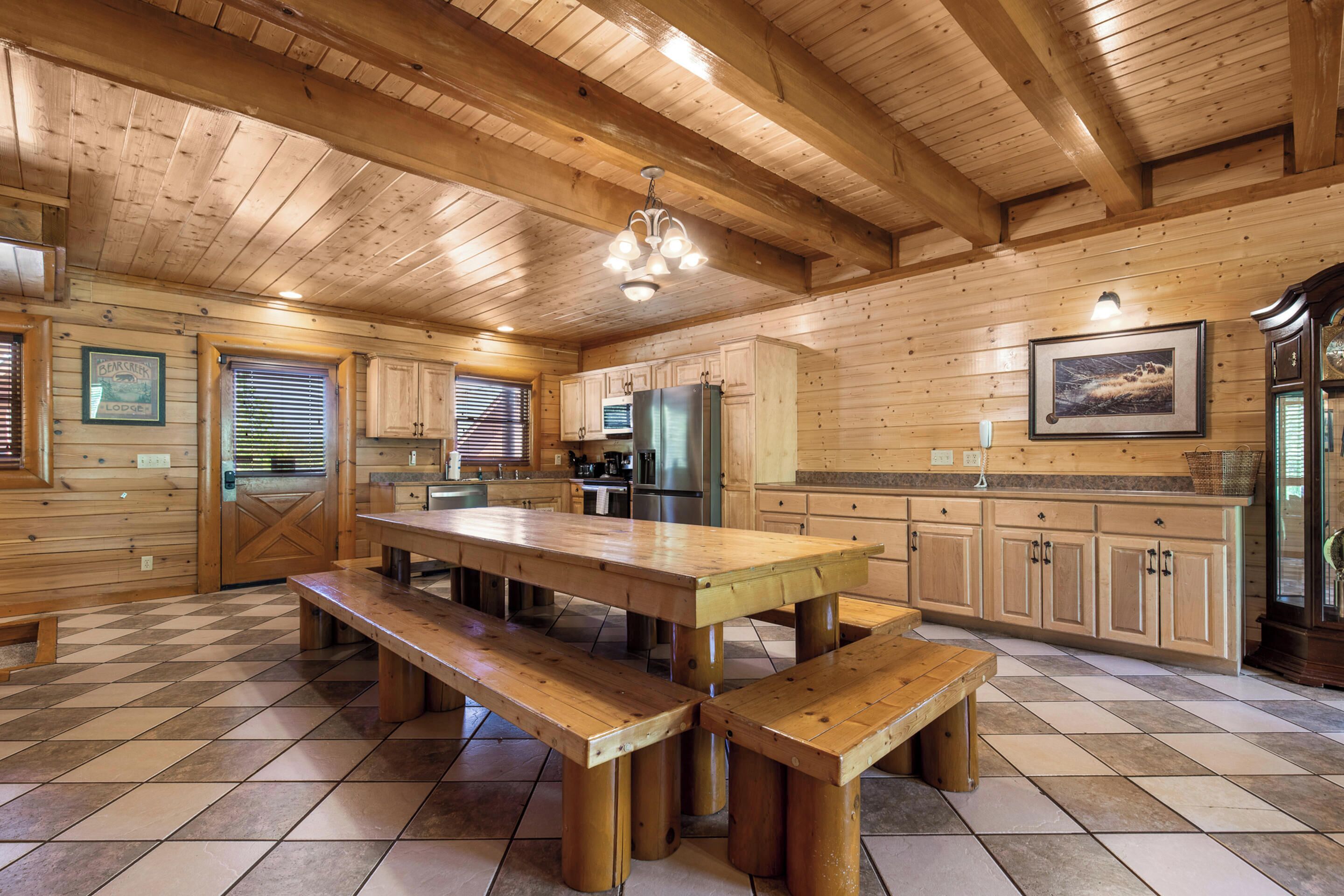A wooden cabin with a large dining table and benches, wooden walls, and a tiled floor.
