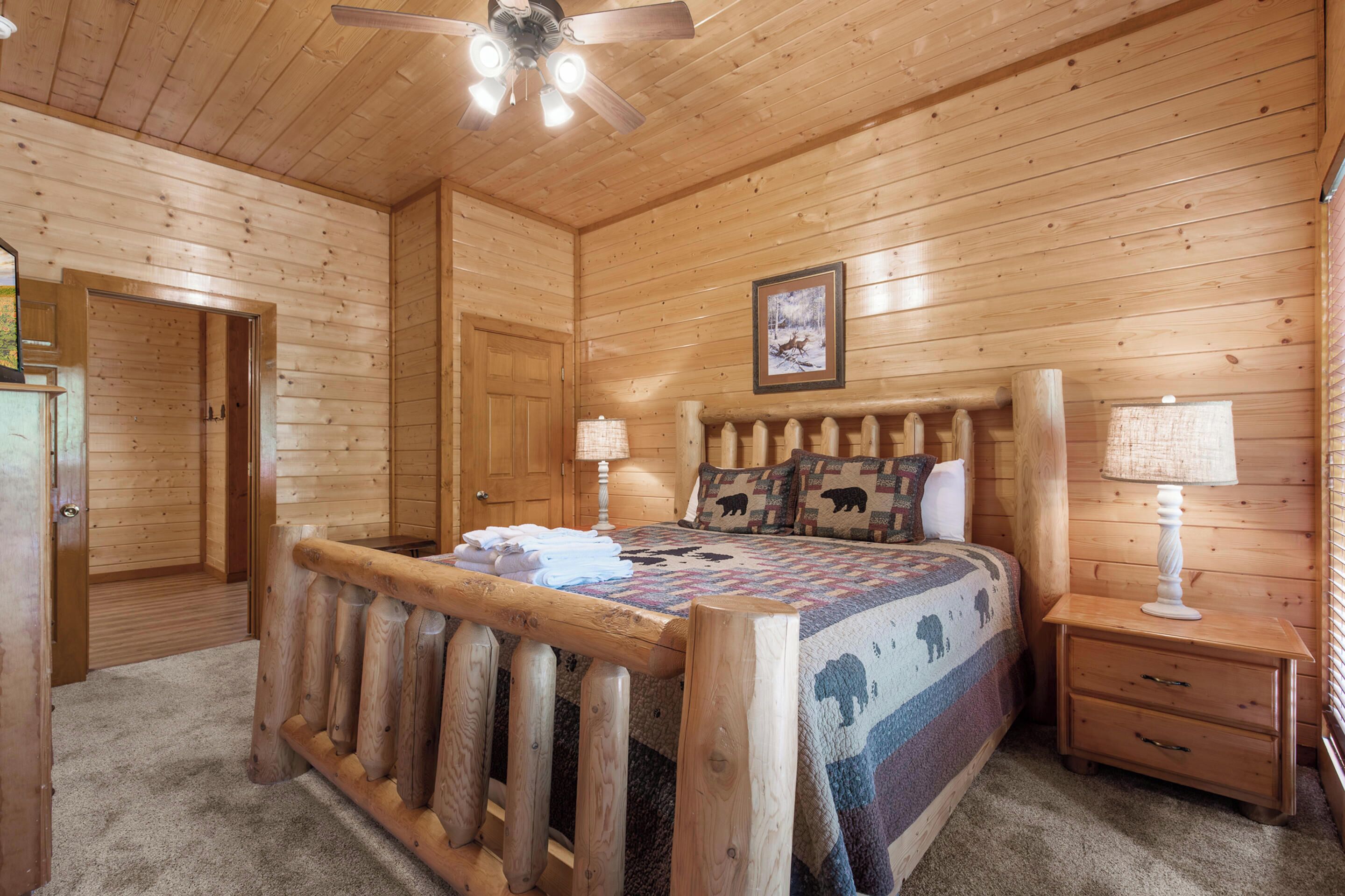 A wooden cabin bedroom with a bed, nightstands, a ceiling fan, and a framed picture on the wall.