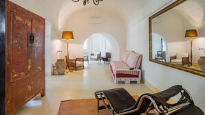 A spacious room with a large arched doorway, a wooden cabinet, a bed with striped bedding, two lounge chairs, and a large mirror on the wall. - Leu075 in Castrignano del Capo (Castrignano del Capo)