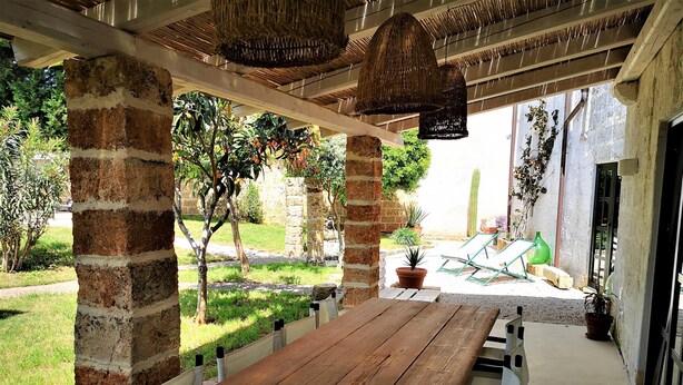 A wooden bench under a covered area with hanging baskets, brick pillars, and potted plants. - Leu075 in Castrignano del Capo (Castrignano del Capo)