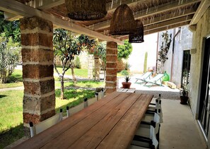 A wooden bench under a covered area with hanging baskets, brick pillars, and potted plants. - Leu075 in Castrignano del Capo (Castrignano del Capo)