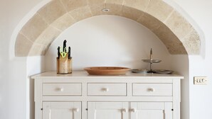 A kitchen with a white cabinet under an arched stone ceiling, a wooden knife block, a terracotta bowl, and a metal serving tray.