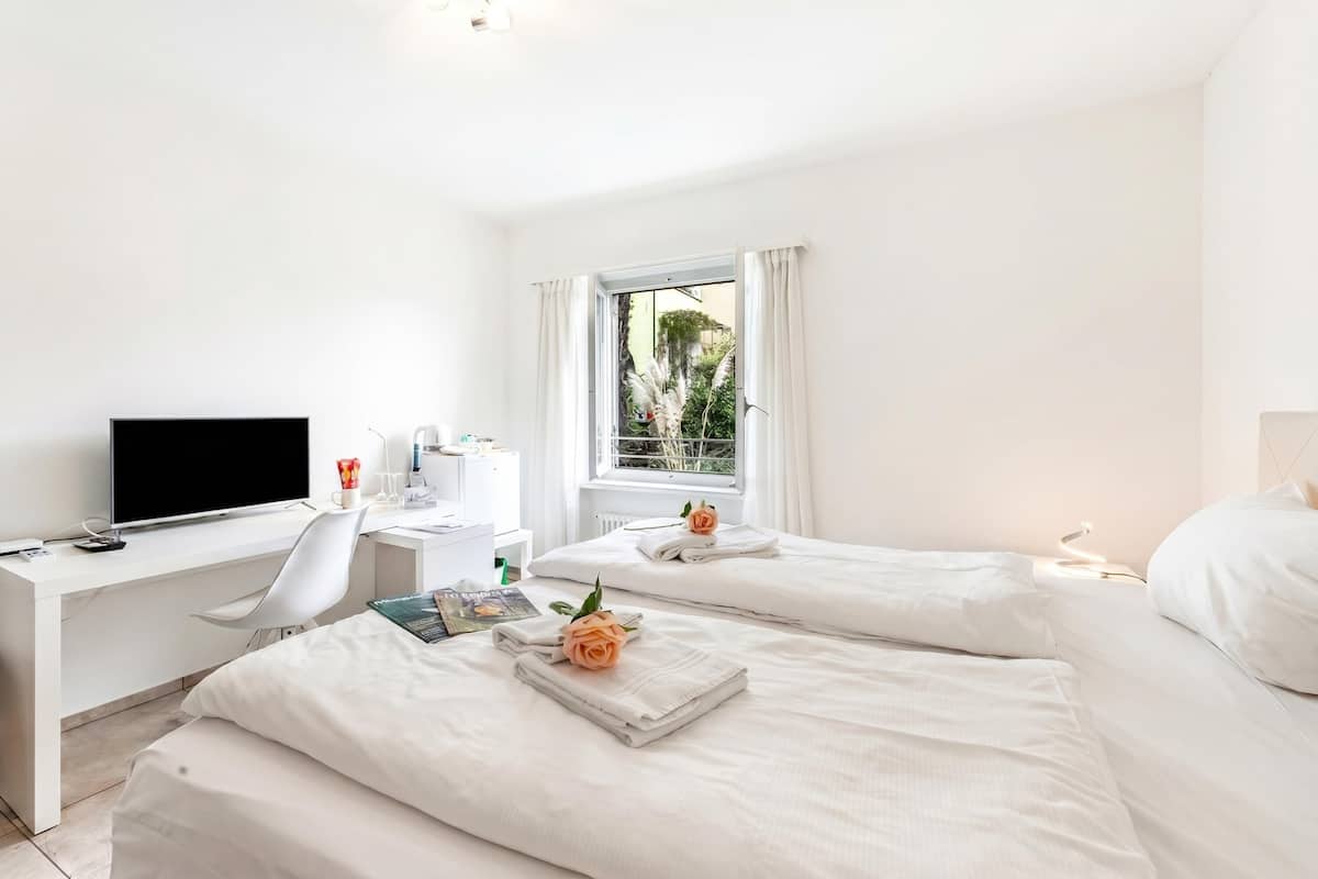 Habitación de hotel con dos camas, un escritorio con televisor y una ventana con cortinas.