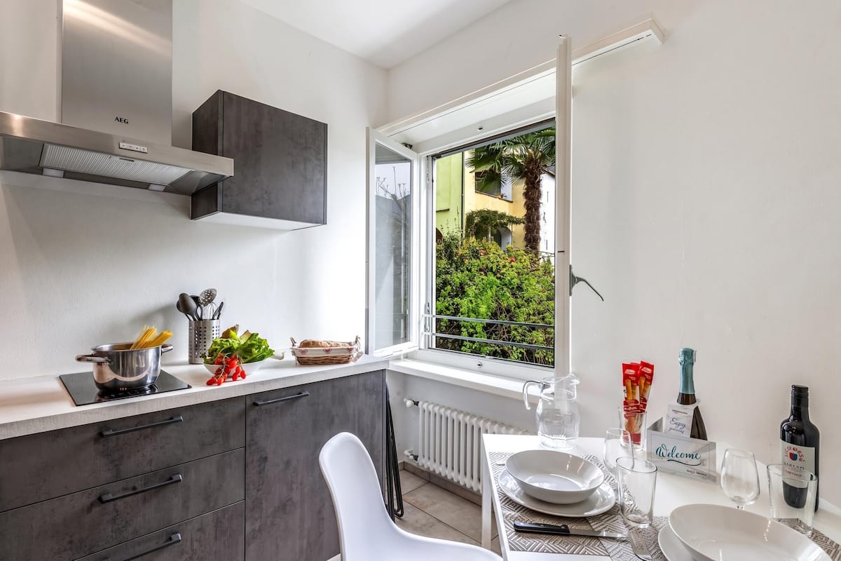 Una cocina moderna con estufa integrada, ventana con vistas a la vegetación y comedor para dos personas con mesa y sillas.