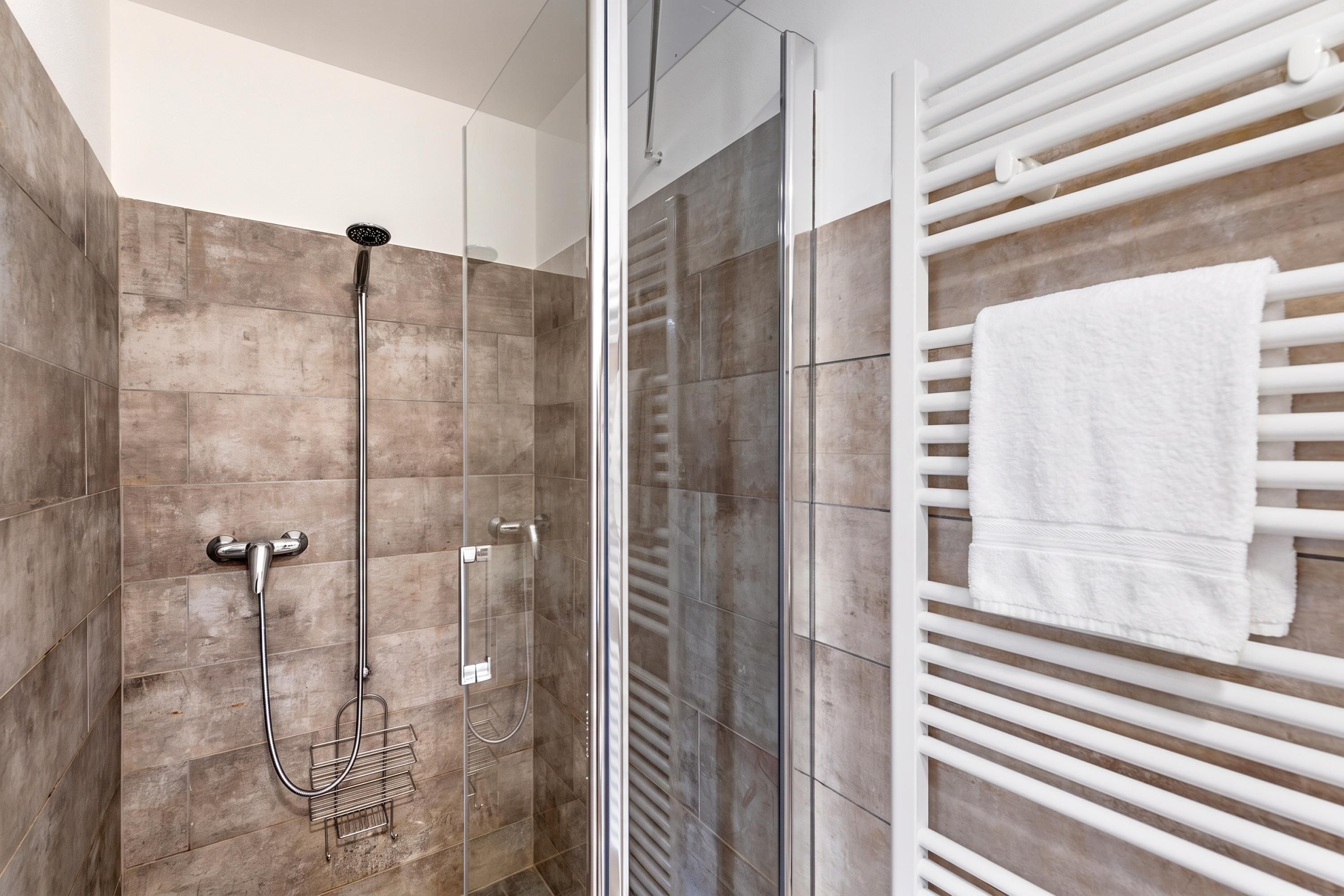 A modern bathroom with a glass shower enclosure, a white towel rack, and a shower control panel.