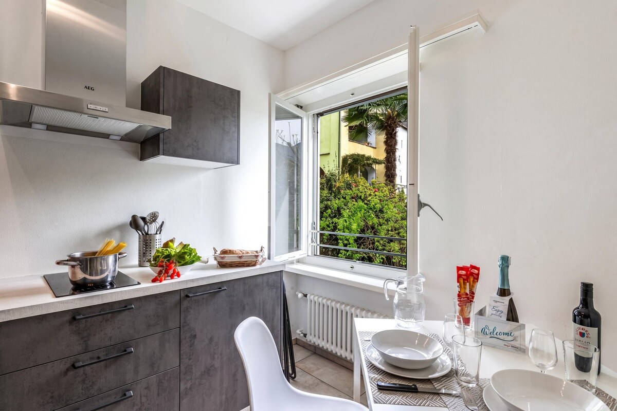 A modern kitchen with a built-in stove, a window with a view of greenery, and a dining area with a table set for two.