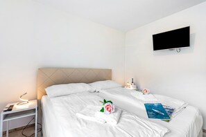 A hotel room with two beds, a TV mounted on the wall, a bedside table with a lamp, and a magazine on the bed. - Residenza La Serenata (Terre di Pedemonte)