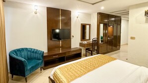 A hotel room with a large bed, a TV mounted on the wall, a desk with a chair, and a wardrobe. - Oban Hotel Multan- Managed by GOHO (Multan)