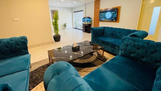 A modern living room with a teal sofa set, a black marble coffee table, and a flat-screen TV mounted on the wall. - Oban Hotel Multan- Managed by GOHO (Multan)