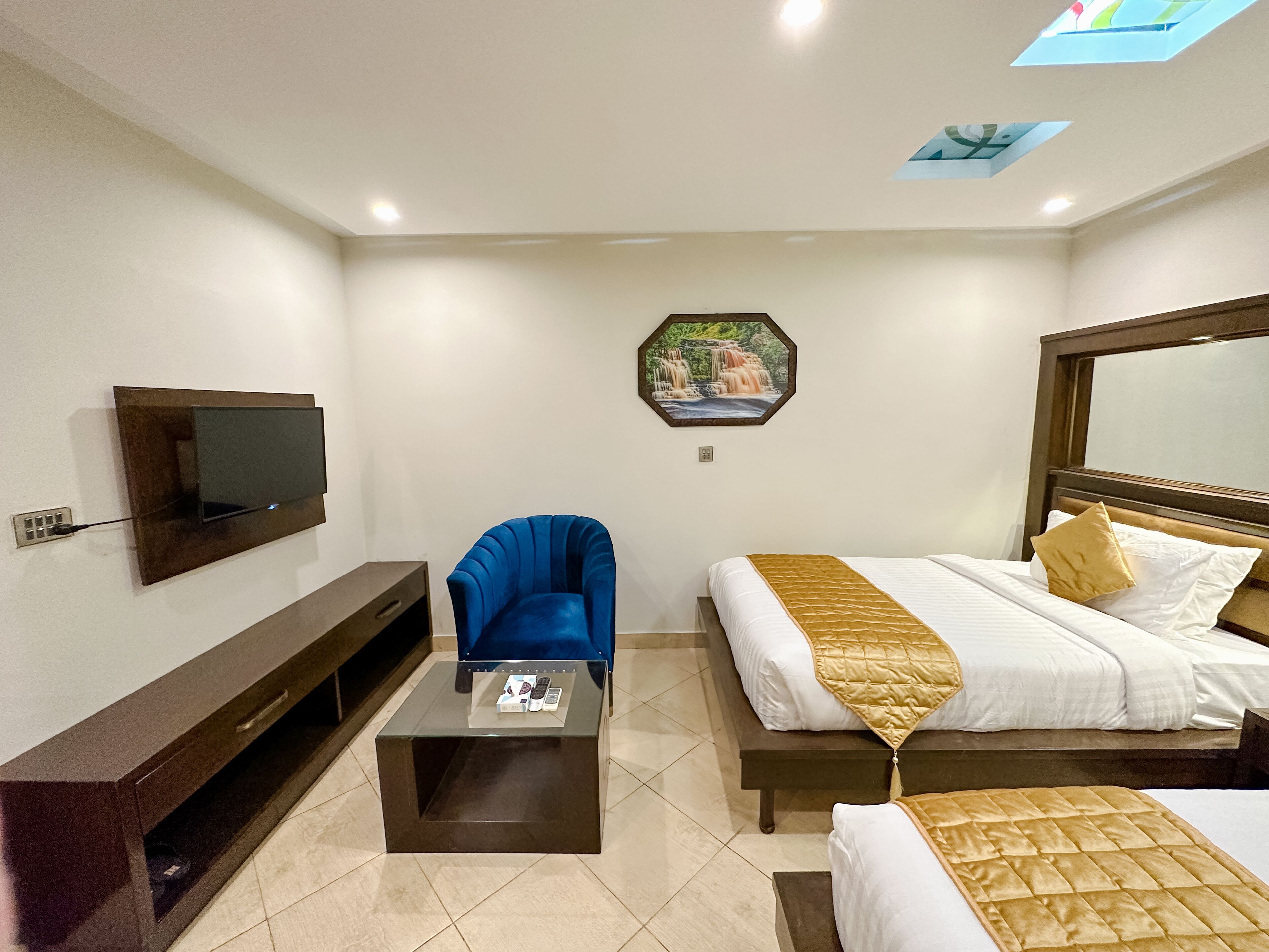 Een hotelkamer met een bed, een blauwe stoel, een aan de muur bevestigde televisie en een decoratieve wandversiering.