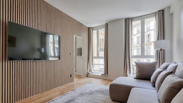 Un salon moderne doté d’un grand téléviseur à écran plat, d’un canapé, d’un tapis à motifs et d’un panneau mural en bois.