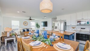 A modern kitchen with white cabinets, a microwave, and a stove. There is a dining table set with blue glassware and white napkins. - Birds of Paradise by Ryson Vacation Rentals (Freeport)