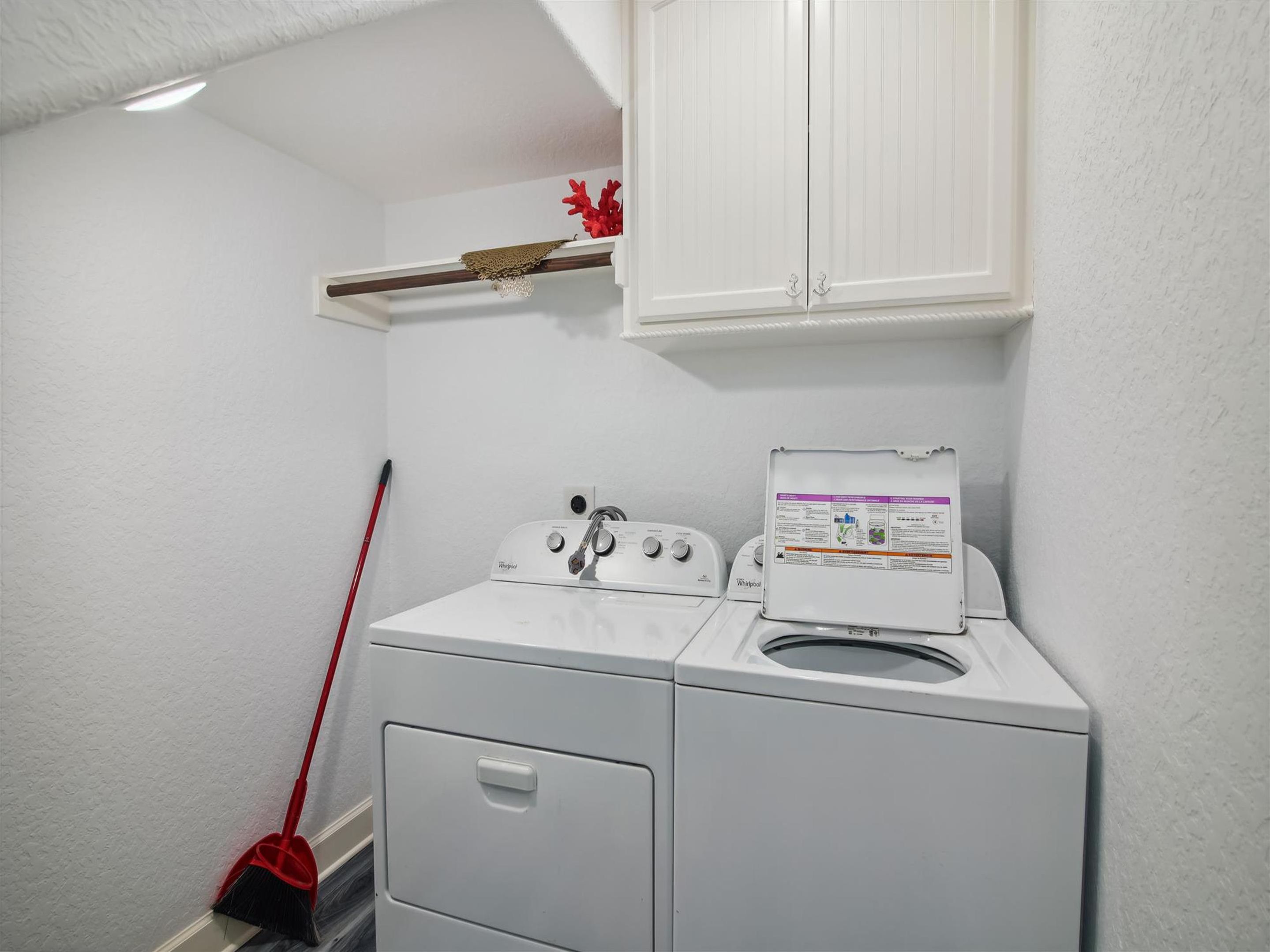 A laundry room with a front-loading washer and dryer, a mop, and a cabinet above the dryer.