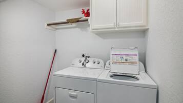 A laundry room with a front-loading washer and dryer, a mop, and a cabinet above the dryer.
