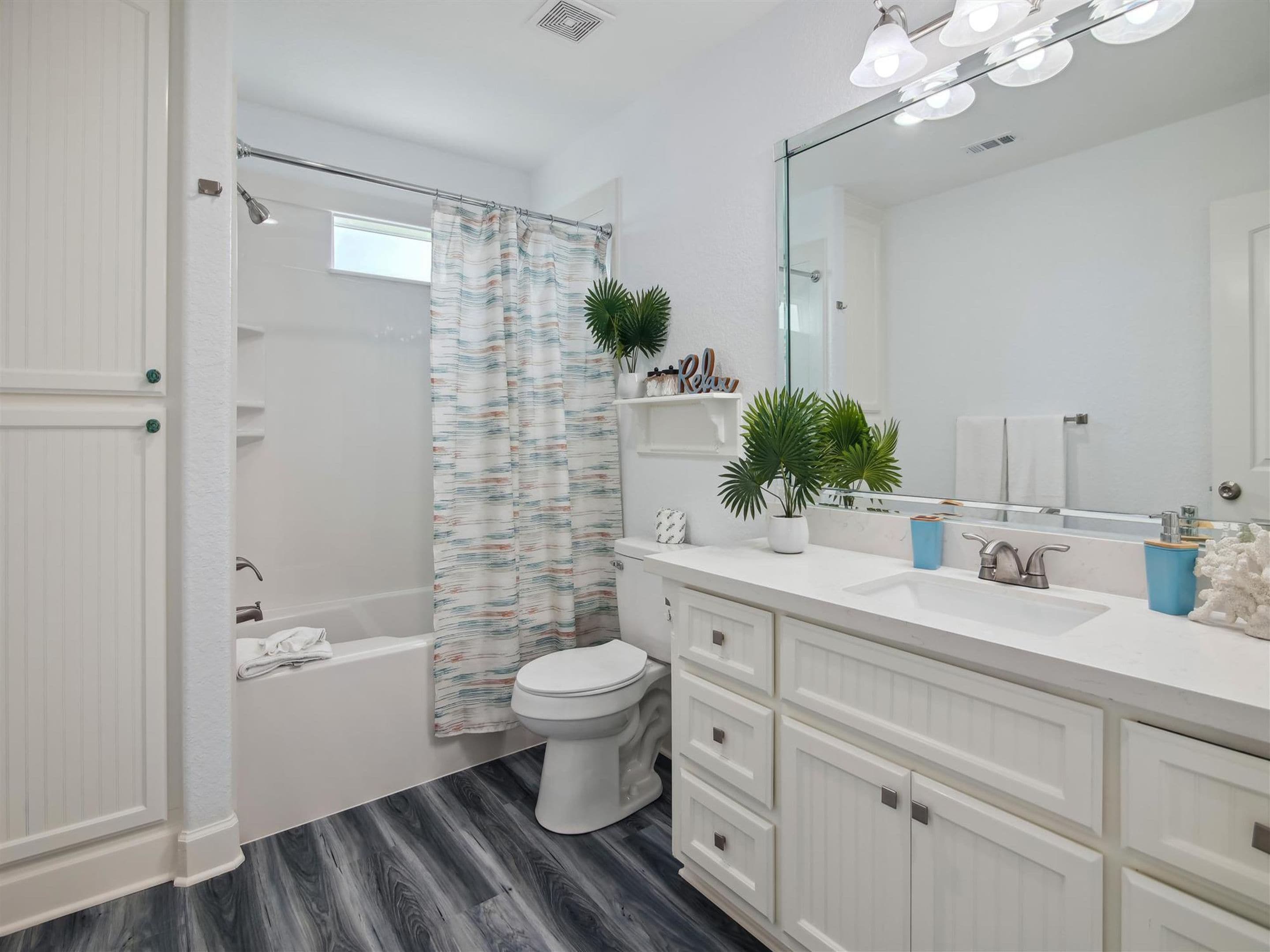 A modern bathroom with a shower, toilet, and vanity with a large mirror and multiple drawers.