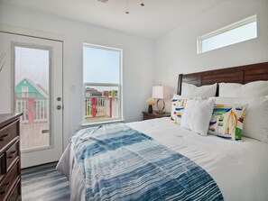 A hotel room with a large bed, a nightstand, a lamp, and a view of buildings through the window. - Birds of Paradise by Ryson Vacation Rentals (Freeport)