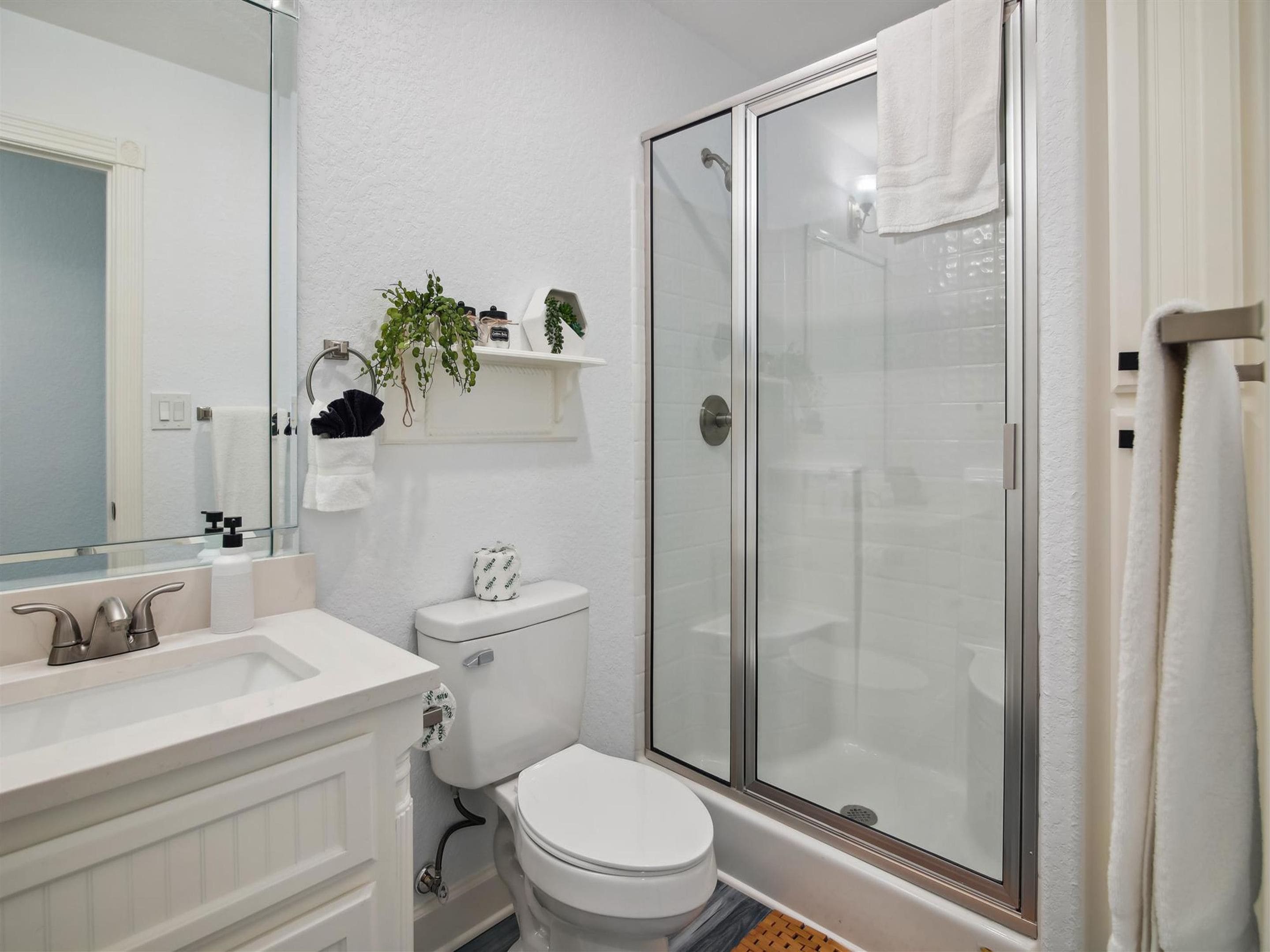 Un baño moderno con ducha envuelta en vidrio, inodoro blanco y tocador con espejo.