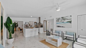 Un salon moderne avec un sol en marbre, des canapés blancs, une table basse et un coin repas avec une cuisine en arrière-plan.