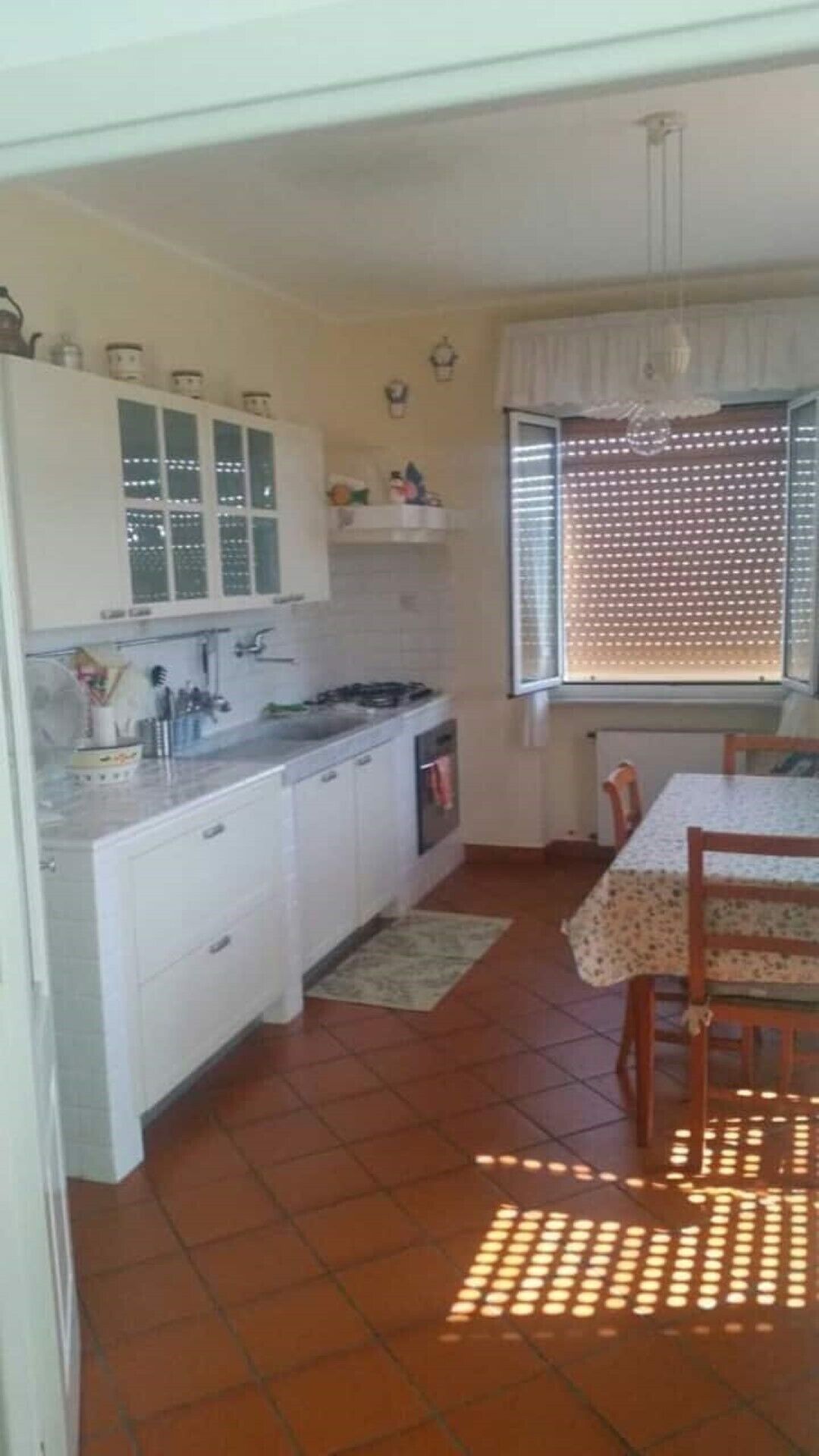 Cozinha compacta com armários brancos, fogão e área de refeições com mesa e cadeiras.